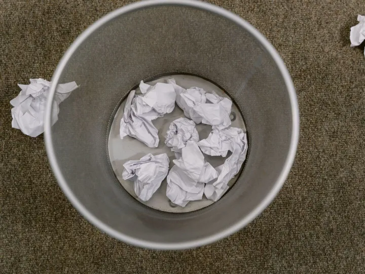 A wastepaper basket filled with crumpled sheets of paper