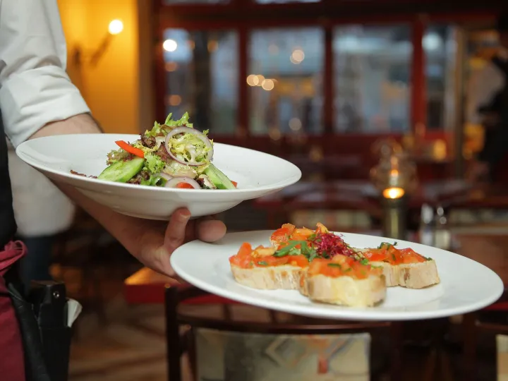 A waiter carrying plates of salad and bruschetta in a restaurant