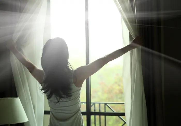 woman opening curtains at window