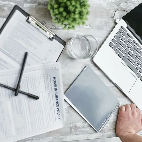 Person Writing on White Paper Beside Clear Glass Mug and Silver Macbook