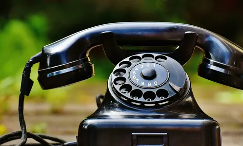 Close-up of a classic black rotary phone outdoors with a blurred green background.