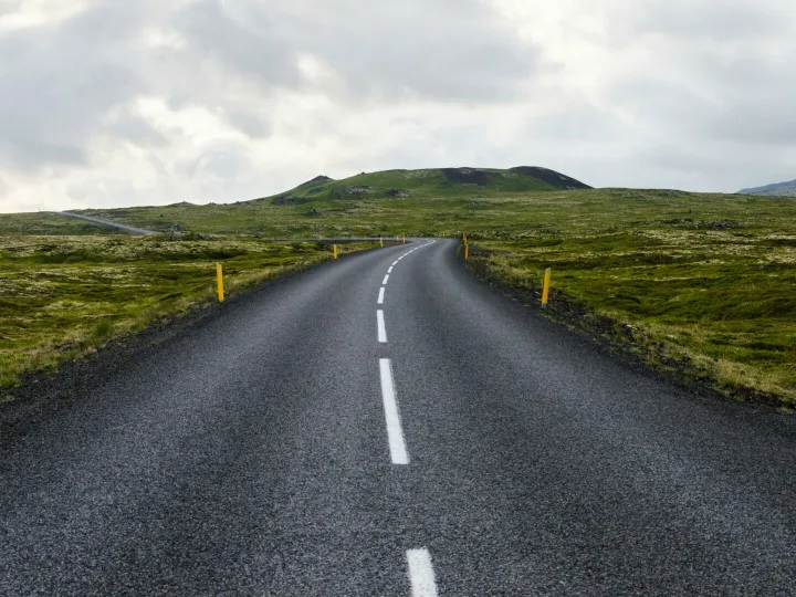 Empty road stretches through lush countryside under cloudy skies, ideal for travel themes.