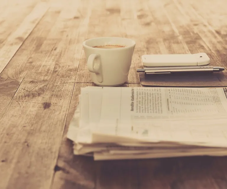A warm vintage morning setup with coffee, newspaper, and smartphone on wooden table.