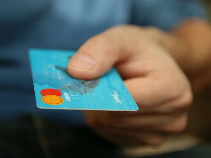 A close-up shot of a hand offering a blue debit card for payment.