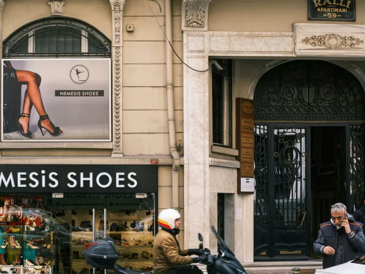 Urban street view with Nemesis Shoes boutique, pedestrians, and scooter, capturing daily city life.