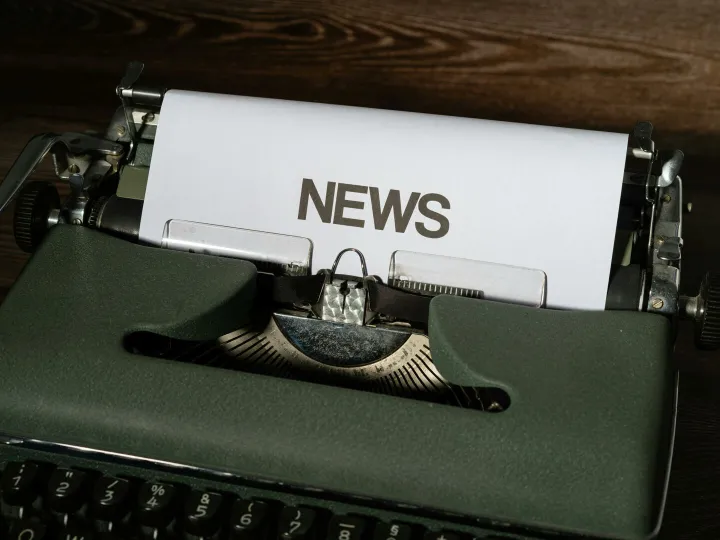 A retro typewriter featuring a 'NEWS' headline typed on white paper against a wooden surface.