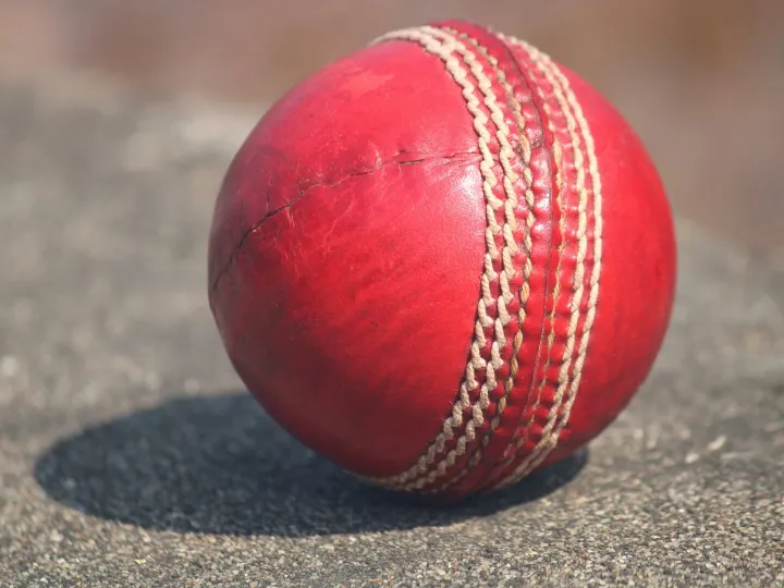 Detailed view of a textured red cricket ball outdoors in sunlight.