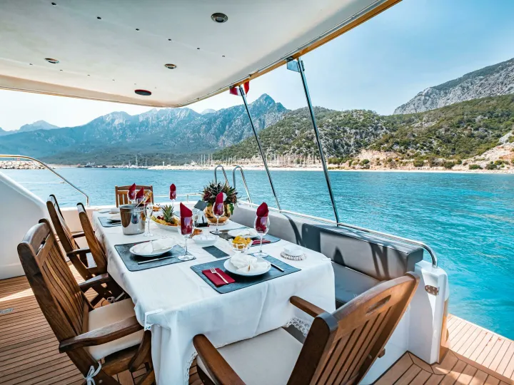 Elegant dining setup on a yacht overlooking Antalya's scenic coast in T&uuml;rkiye.