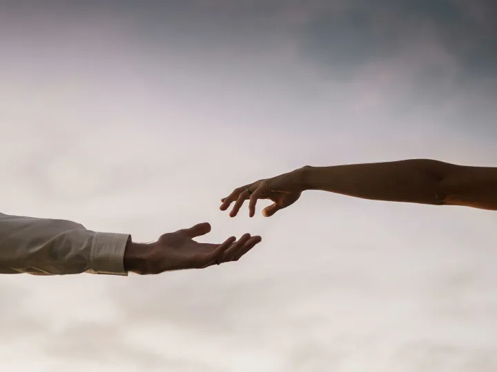Two hands reaching towards each other against a soft twilight sky symbolizing connection and love.