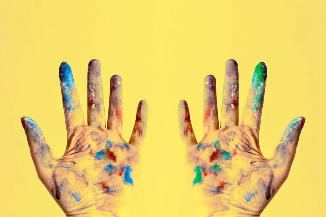 A child's paint-covered hands raised against a yellow background