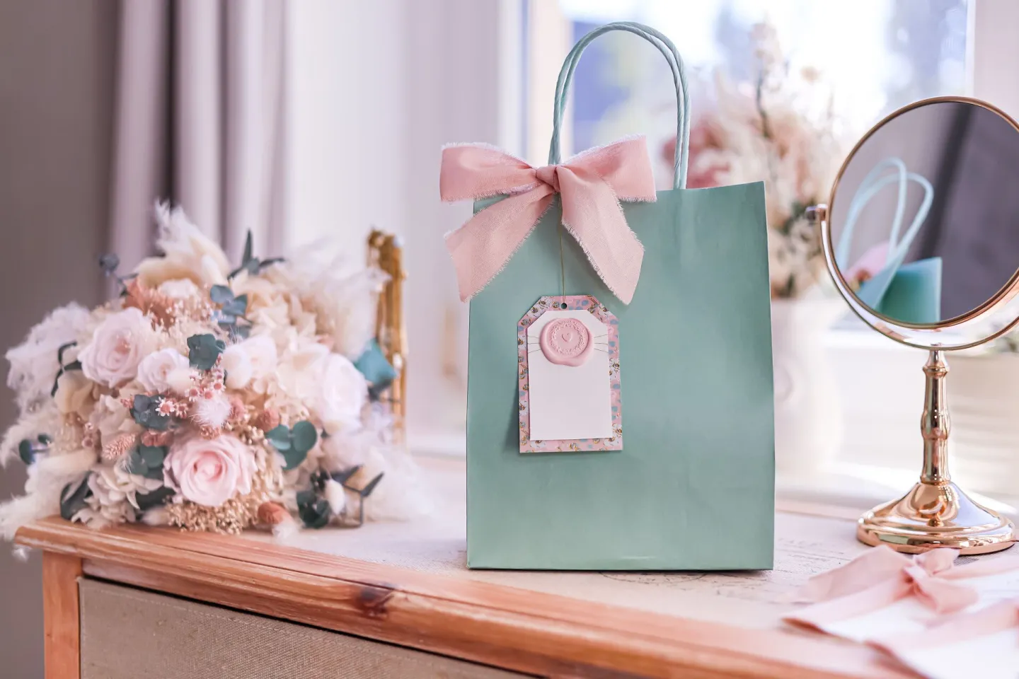 A gift bag tied with a ribbon beside a pastel flower arrangement