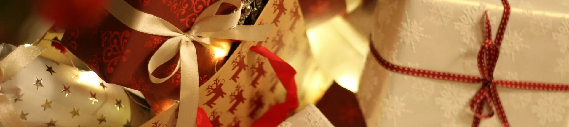 Beautifully wrapped Christmas presents under the tree with festive decorations and ribbons.