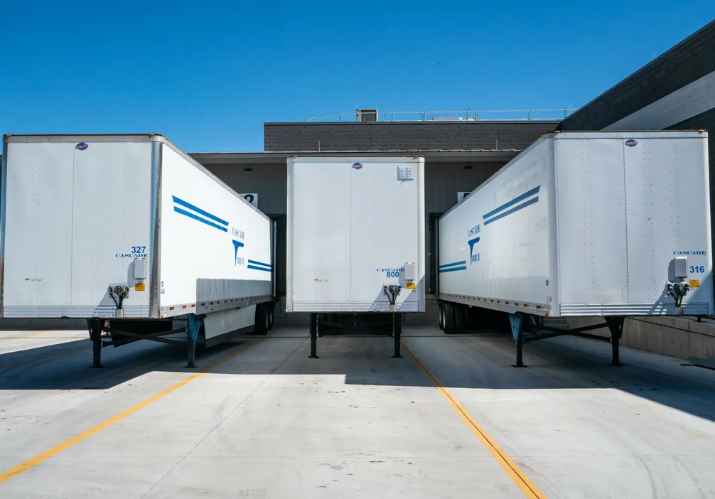 Three white cargo trailers parked at an industrial shipping dock under clear blue skies.