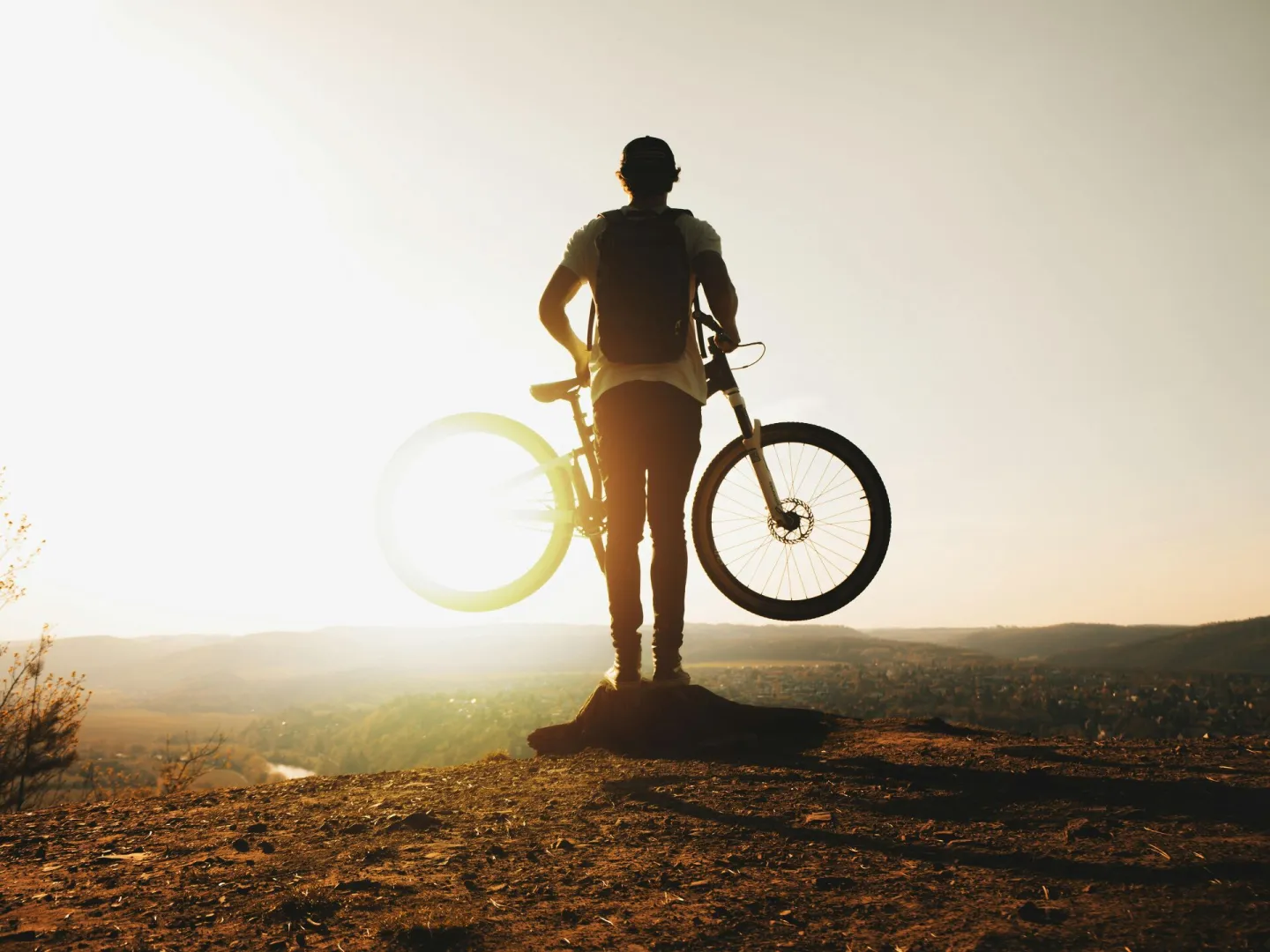 A cyclist stands silhouetted with a mountain bike