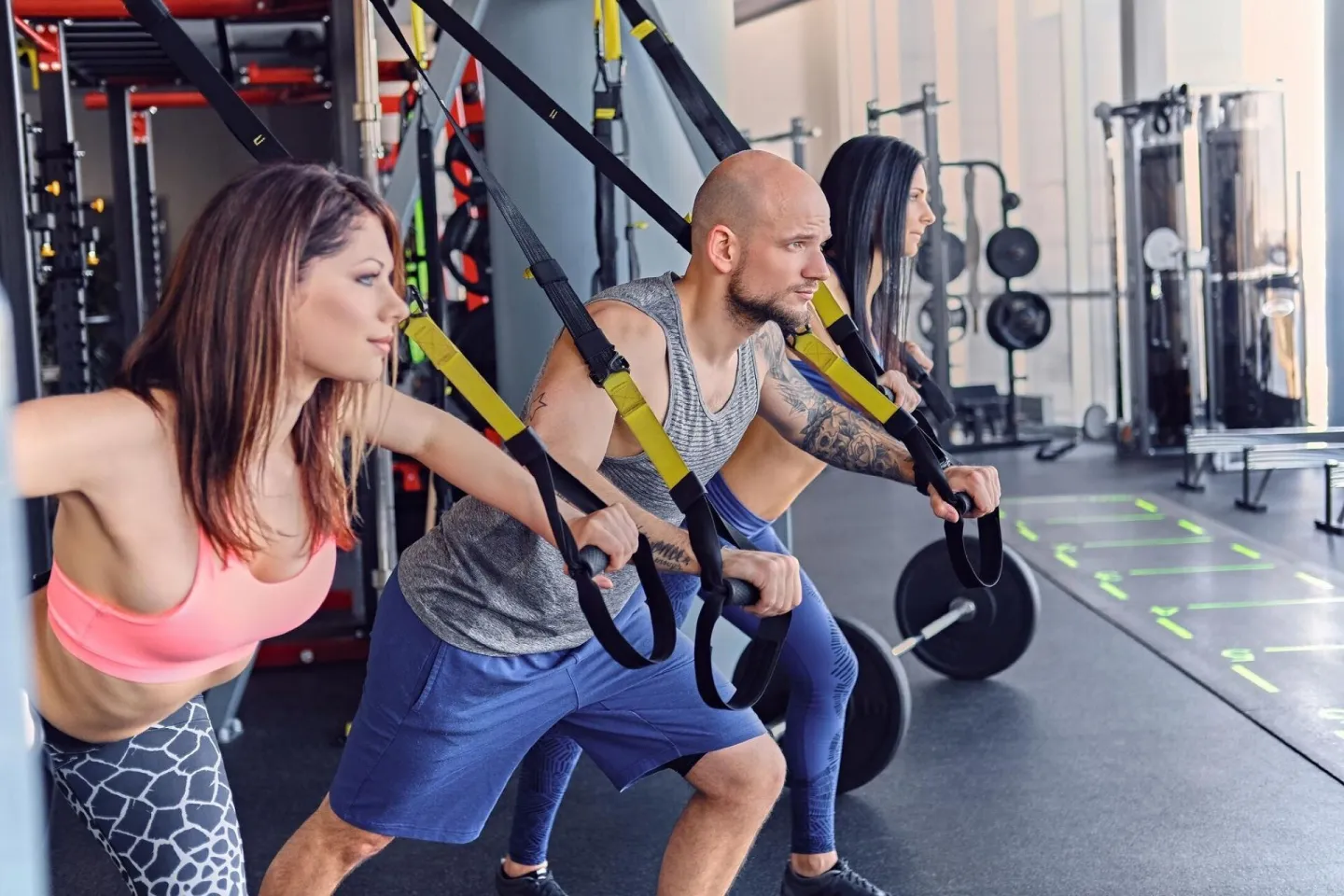 Athletic tattooed male and two sporty women doing trx straps