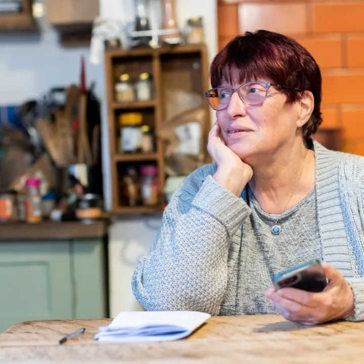 A woman sitting at a kitchen table holding a mobile phone and considering what to make of it