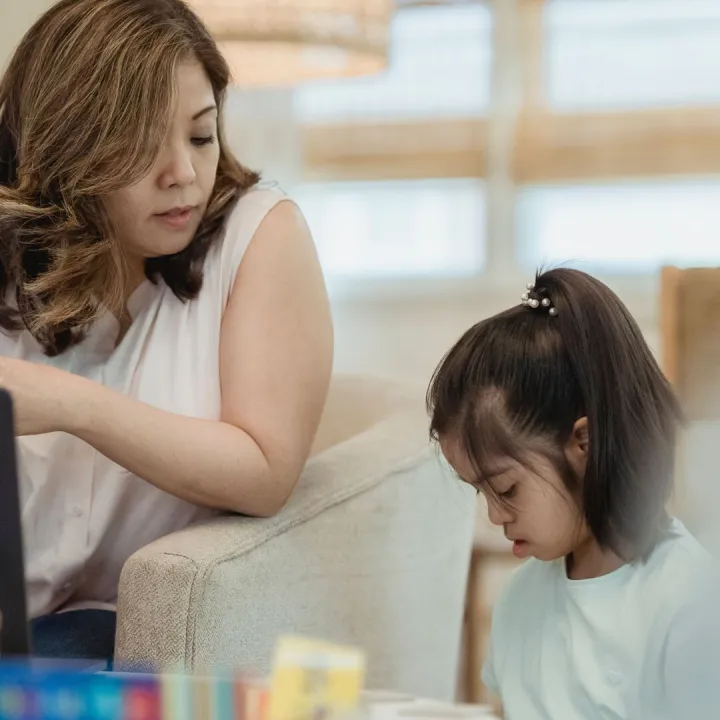 Parent looking at her phone at home while her young daughter plays beside her