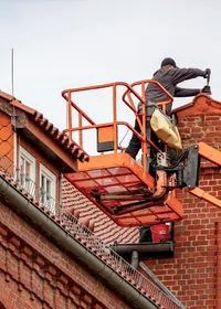 Roofer on a cherry picker repairing a tiled roof on a red brick building