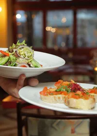 A waiter carrying plates of salad and bruschetta in a restaurant