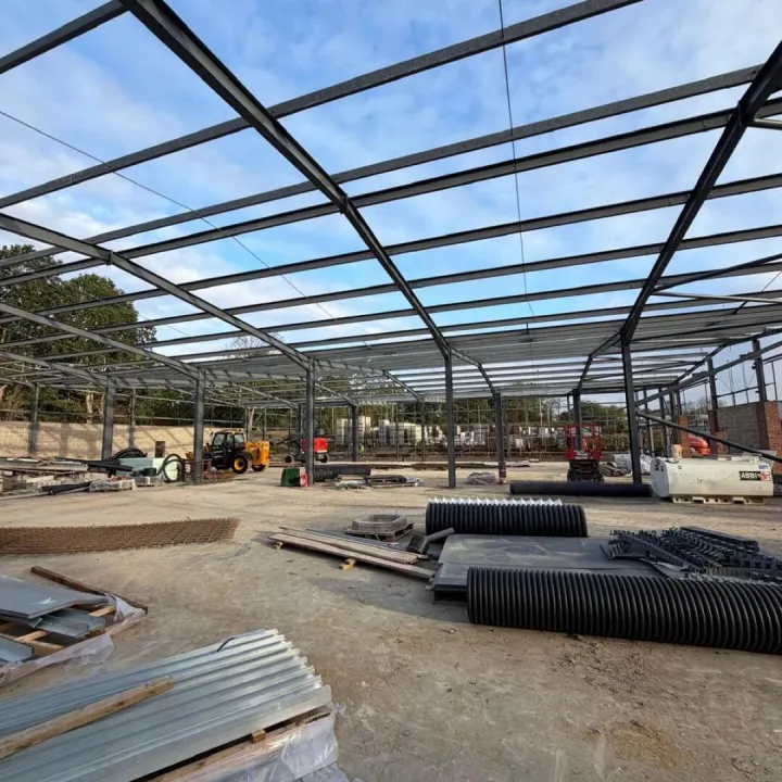 Dark painted steel portal frame against a blue sky, with roof sheets and drainage pipe on the slab below