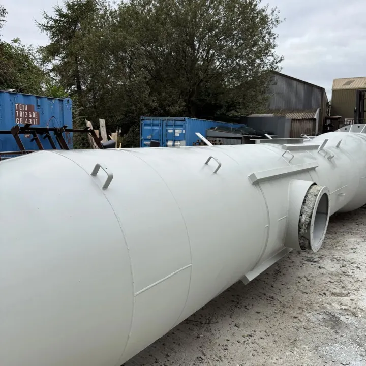 Primed light grey steel chimney section with lifting lugs and a round side port, laid out on a gravel yard