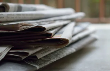 A close-up of a stack of newspapers resting on a desk, symbolizing information and media.