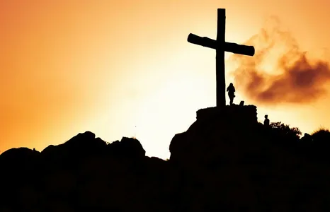 Majestic silhouette of a cross on a hill during a vivid sunset, symbolizing spirituality.