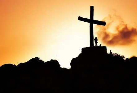 Majestic silhouette of a cross on a hill during a vivid sunset, symbolizing spirituality.