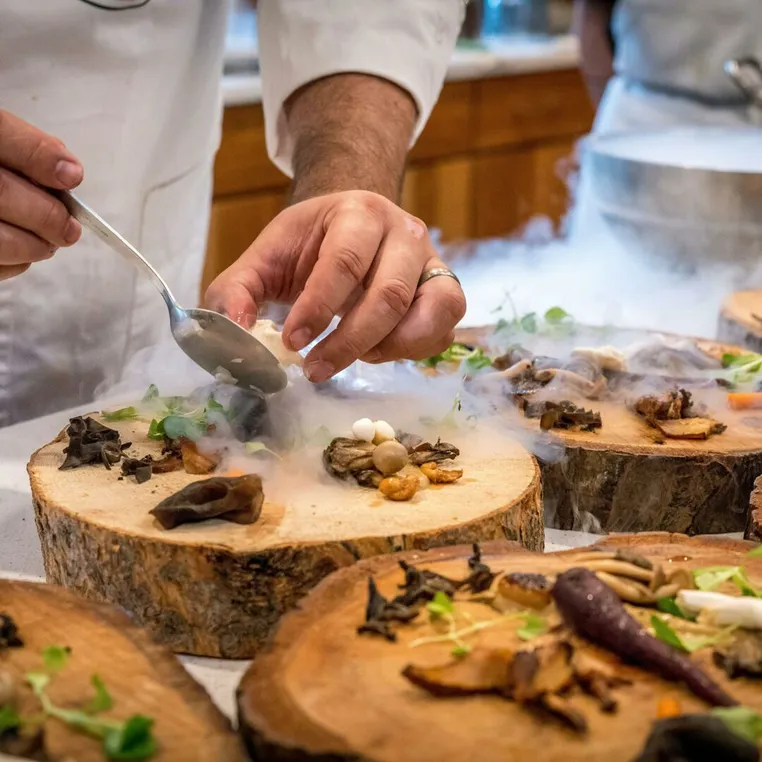 A chef plating dishes on wooden rounds, with dry-ice smoke