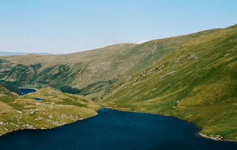 Aerial view of a tranquil lake surrounded by rolling hills in England's Lake District.