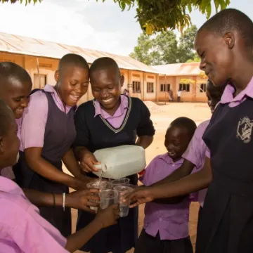 Children at St Balikuddembe school enjoying water from their new tank &ndash; Copyright All We Can