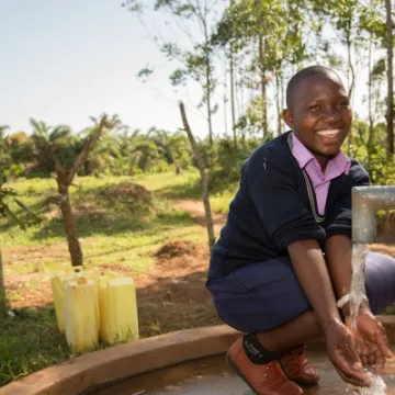 Prossy Nabiryo chair of St Balikddembe schools health club (SHC) using a new community water pump – Copyright All We Can
