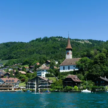 A picturesque view of Spiez, Switzerland with the iconic church and Lake Thun under a clear blue sky.