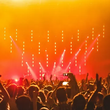 Energetic crowd at a live concert with bright stage lights and hands raised in celebration.