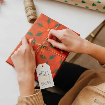 Hands wrapping a red Christmas gift with a 'Holly