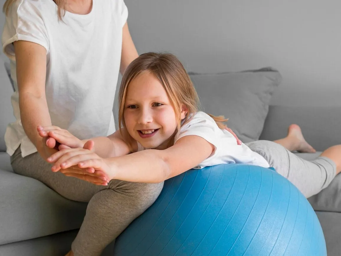 Mom helping girl to exercise on ball