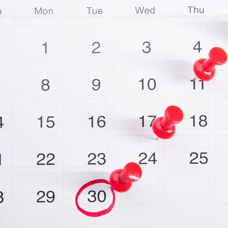 Close-up of a calendar with red push pins marking