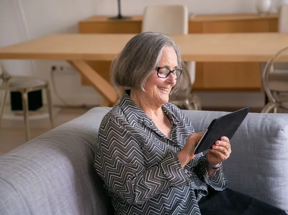An older resident smiling as she reads her parish council website on a tablet at home