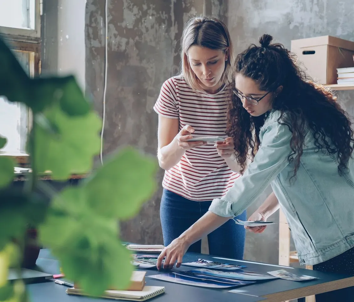 Two women looking over printed designs laid out on a table