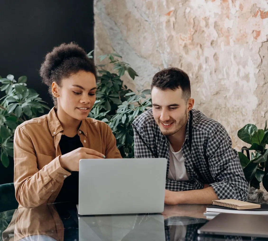 Two colleagues sitting together looking at the same laptop screen