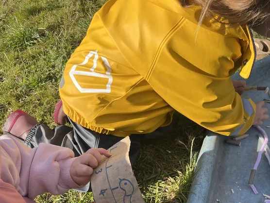 Two children threading wool through the numbers carved into a wooden board