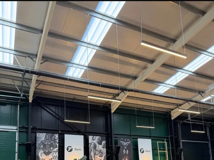 Gym hall with dark green and black painted walls, exposed roof trusses and rows of strength machines