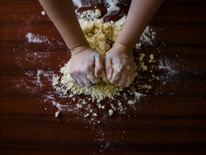 Hands kneading dough on a floured wooden worktop