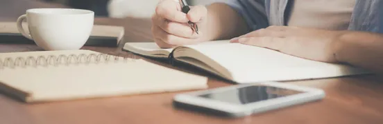 Woman Writing on a Notebook Beside Teacup and Tablet Computer