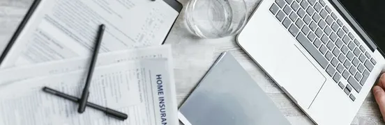 Person Writing on White Paper Beside Clear Glass Mug and Silver Macbook