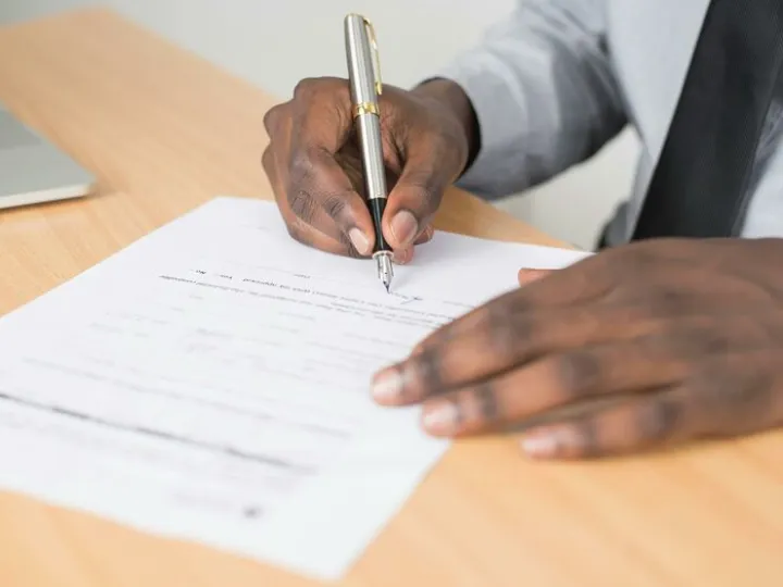 Person Holding Gray Twist Pen and White Printer Paper on Brown Wooden Table