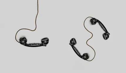Two vintage black telephone handsets connected by cords on gray background.