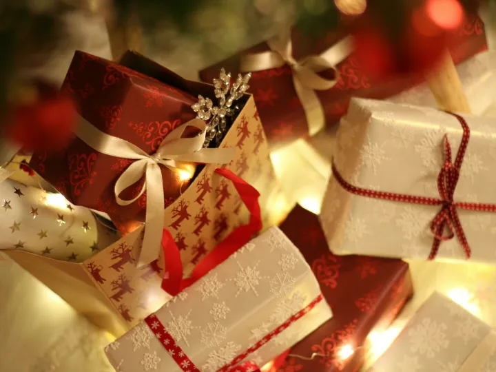 Beautifully wrapped Christmas presents under the tree with festive decorations and ribbons.