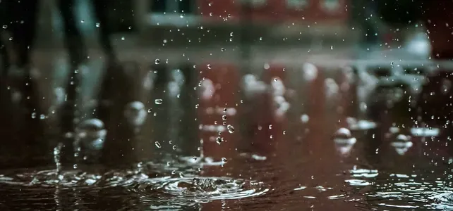 Close-up of raindrops splashing into a puddle, capturing reflections and textures in an outdoor urban setting.