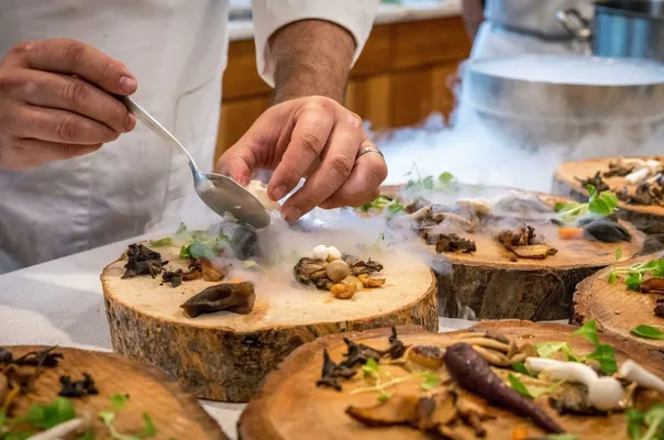 A chef artfully plating a gourmet dish with mushrooms and greens on wood slices.